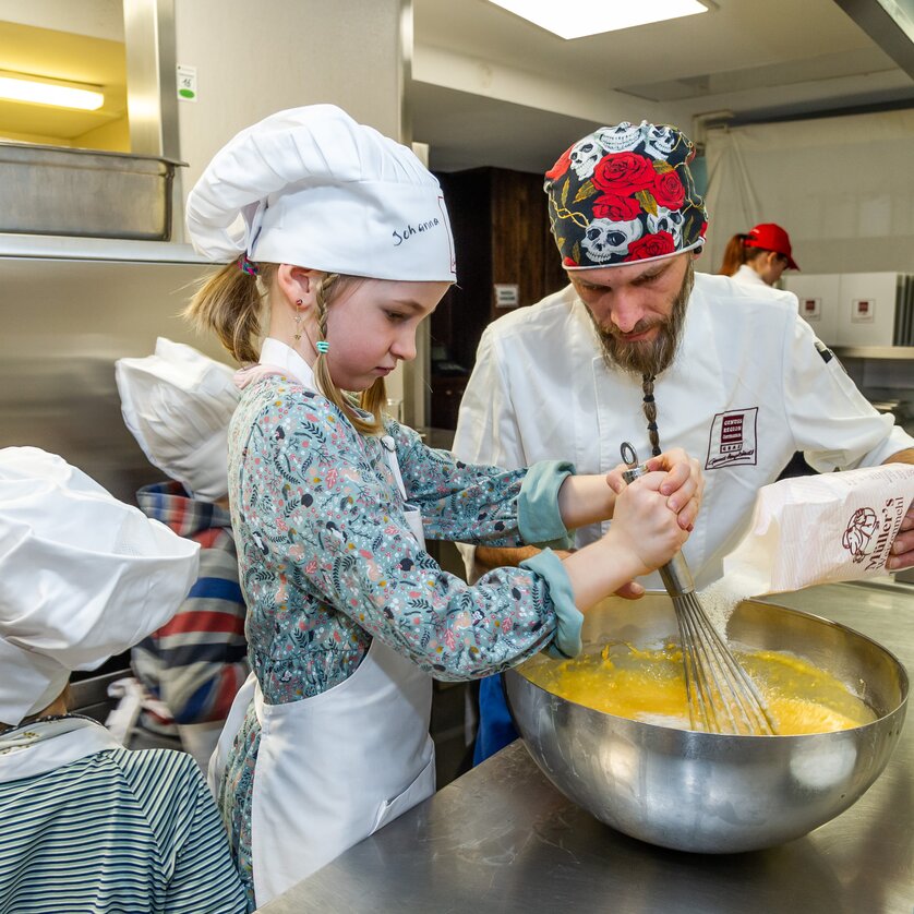 Kinder und ein Koch bereiten gemeinsam Teig in einer Küche zu. | © Graz Tourismus - Paul Stajan