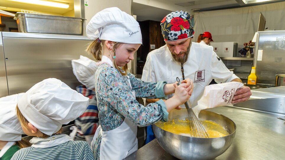 Kinder und ein Koch bereiten gemeinsam Teig in einer Küche zu. | © Graz Tourismus - Paul Stajan