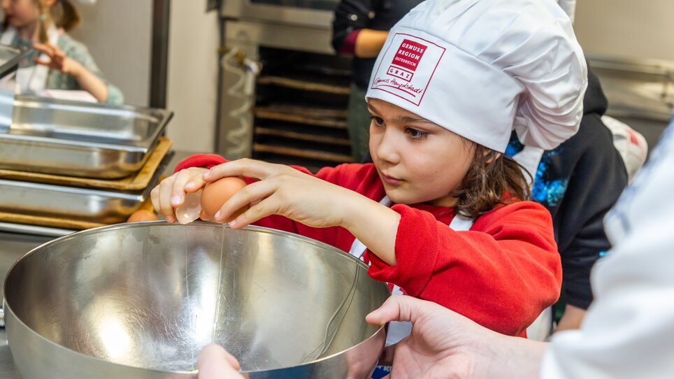 Ein Kind bricht ein Ei in eine Schüssel während eines Kochkurses. | © Graz Tourismus - Paul Stajan