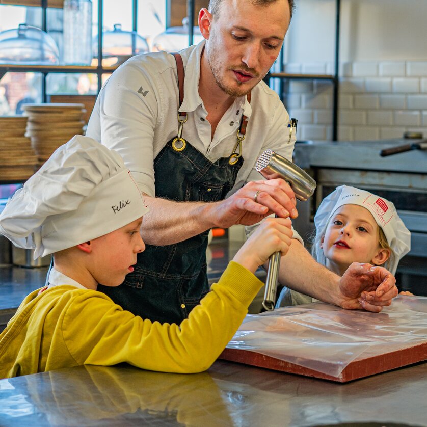 Ein Koch in einer Küche zeigt Kindern bei einem Kochkurs, wie man Teig zubereitet. | © Milena Bonstingl