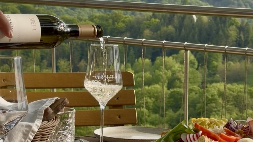 A beautifully set table with wine and various dishes, overlooking the green landscape. | © Schanzlwirt
