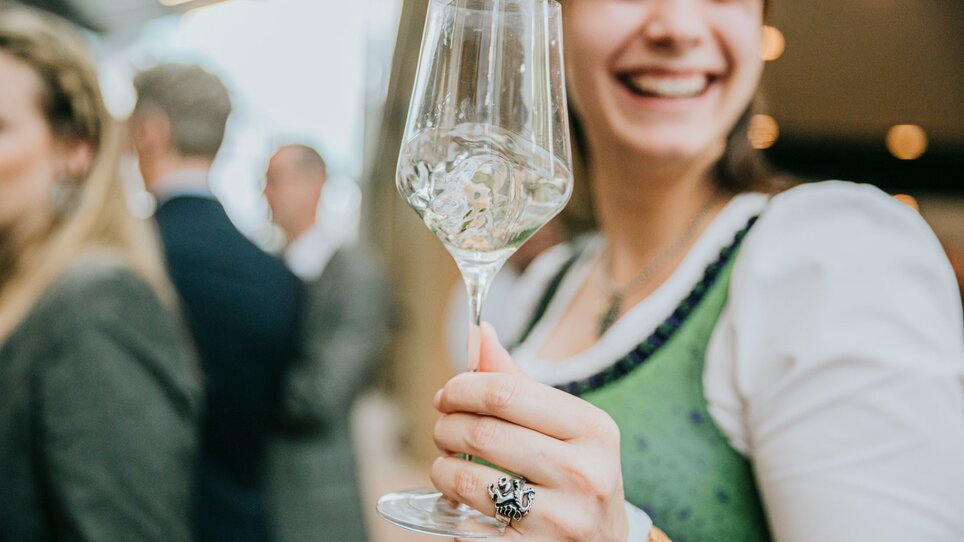 Smiling woman holding a wine glass in a festive setting. | © Wein Steiermark - Johanna Lamprecht