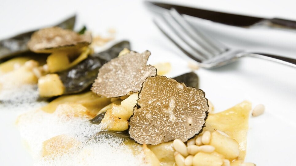 A delicate dish featuring truffles, ravioli, and foam on a white plate. | © Alexander Andreadis