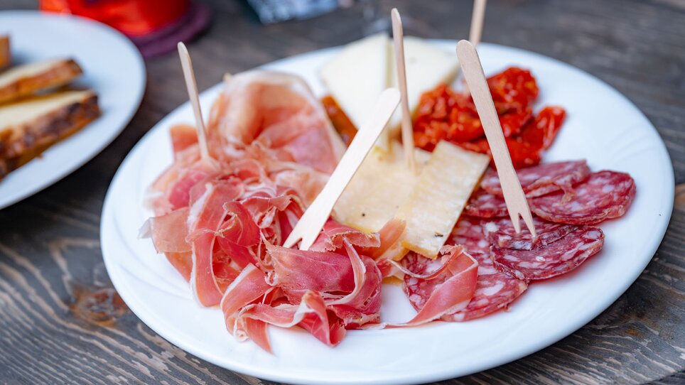 A plate with various types of cured meats and cheeses, alongside dried tomatoes, served with small wooden sticks. | © 5komma5sinne - Rene Strasser (97) kl