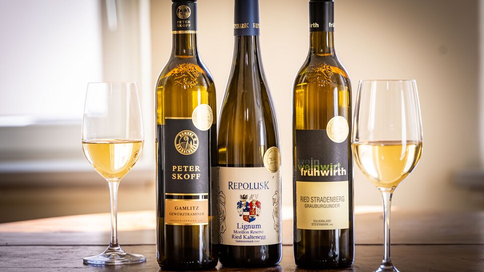 Drei Flaschen Weißwein stehen zwischen zwei Weingläsern auf einem Tisch. | © Graz Tourismus - Werner-Krug