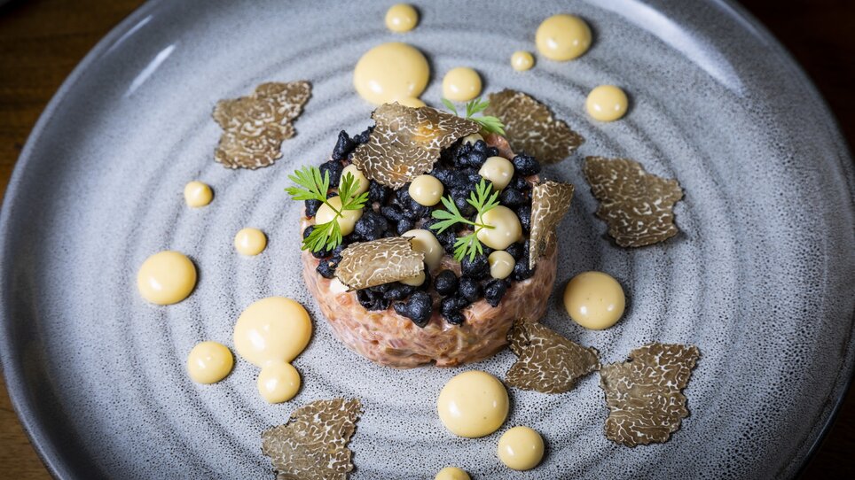 An artistic dish featuring truffles and sauces on a gray plate. | © Graz Tourismus - Werner Krug