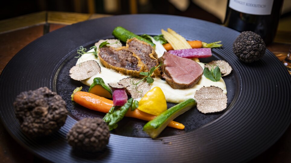 A beautifully plated dish featuring meat, vegetables, and truffles. | © Graz Tourismus - Werner Krug