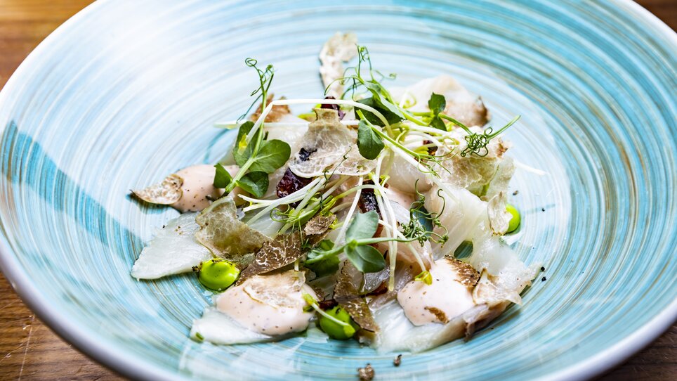 A beautifully arranged truffle salad with various herbs and a creamy sauce on a decorative plate. | © Graz Tourismus - Werner Krug