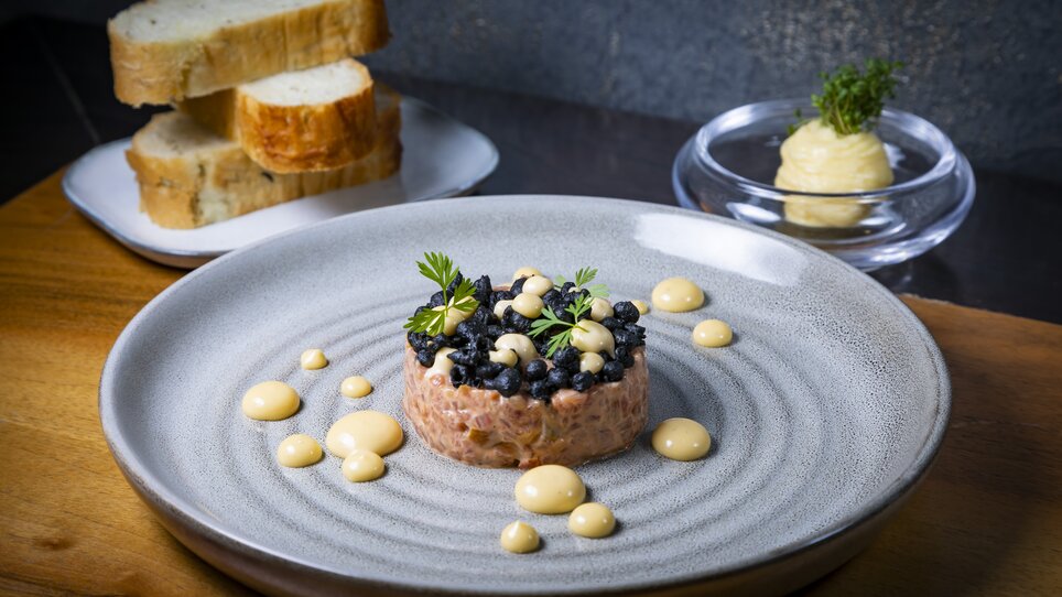 A plate of tartare, blueberries and sauces, enriched with fresh herbs. Fresh bread in the background. | © Graz Tourismus - Werner Krug