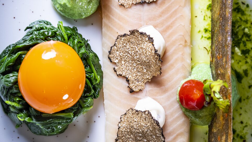 An exquisitely arranged plate featuring fish, truffles, egg yolk, and various garnishes presented elegantly. | © Graz Tourismus - Werner Krug