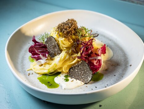 Ein kunstvoll angerichtetes Pastagericht mit Trüffeln, Radicchio und cremiger Sauce auf einem hellen Teller. | © Graz Tourismus - Werner Krug