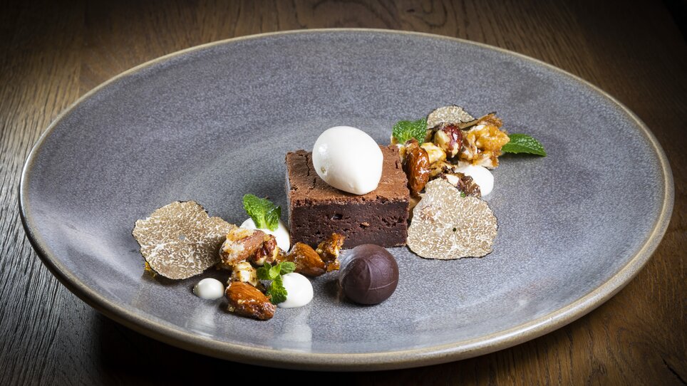 A luxurious dessert featuring brownie, truffles, and ice cream, presented on a gray plate. | © Graz Tourismus - Werner Krug