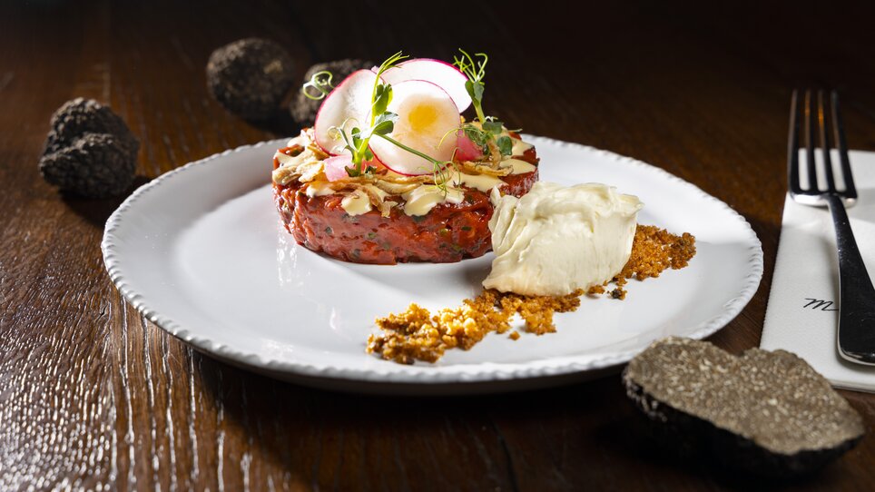 Tatar auf einem Teller, dekoriert mit Radieschen und Kräutern, daneben eine Portion Creme. | © Graz Tourismus - Werner Krug