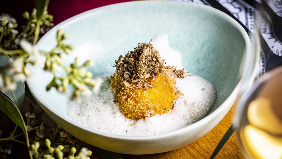 Ein kunstvoll angerichteter Teller mit einer frittierten Trüffel-Kugel auf Schaum. Umgeben von Blumen und Pflanzen. | © Graz Tourismus - Werner Krug