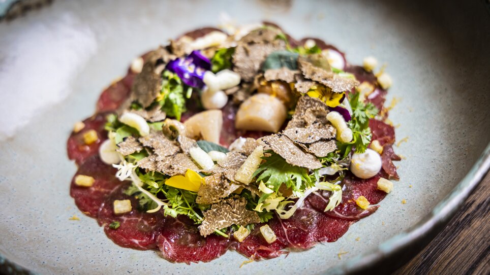 Ein Teller mit exquisitem Rindfleisch-Carpaccio, garniert mit frischen Kräutern, Blumen und Trüffelscheiben. | © Graz Tourismus - Werner Krug