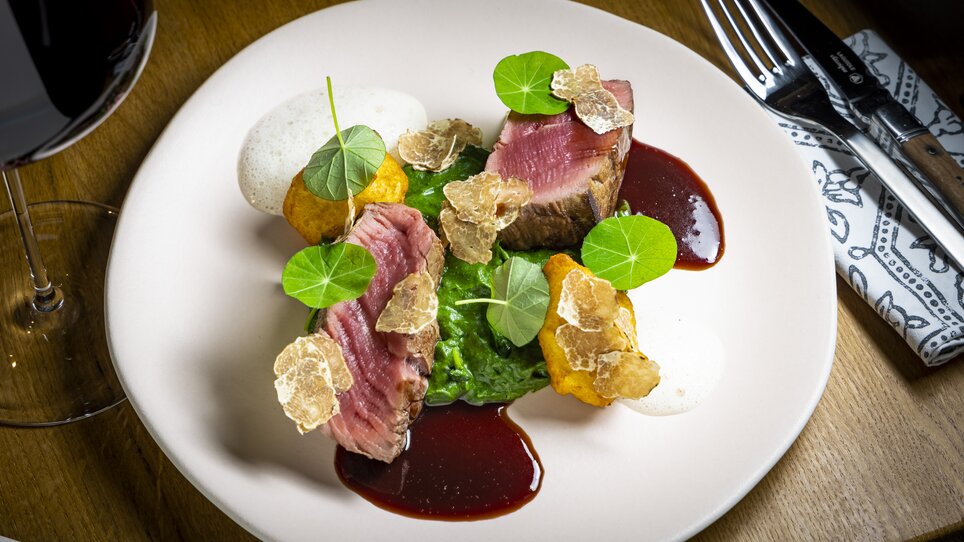 Ein kunstvoll angerichtetes Gericht mit Fleisch, pürierten Erbsen, Sauce, Trüffelstücken und frischen Kräutern. | © Graz Tourismus - Werner Krug