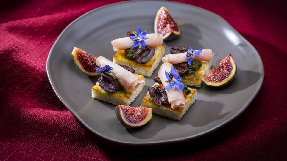 An elegant presentation of small bites with ham, olives, and figs, garnished with edible flowers. | © Graz Tourismus - Werner Krug