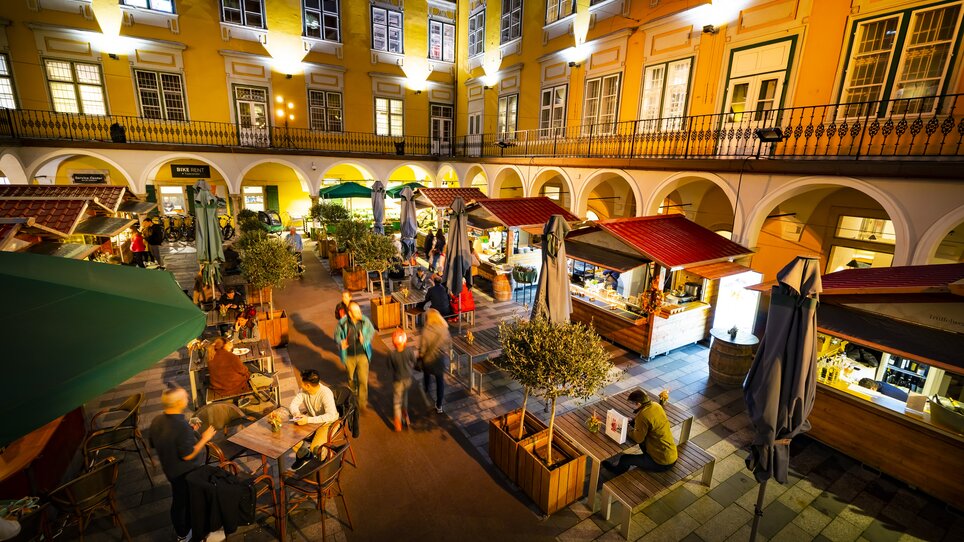 Abendliche Szene eines belebten Trüffelmarkts im Paradeishof in Graz mit Essensständen und Gästen. | © Graz Tourismus - Werner Krug