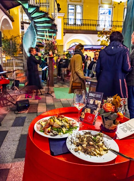 Un tavolo ben apparecchiato con piatti al tartufo, bicchieri e decorazioni floreali. I visitatori godono del festival nel Paradeishof. | © Graz Tourismus - Werner Krug