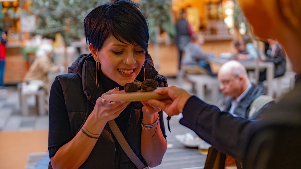 A woman is tasting truffles at an outdoor market. | © 5komma5sinne - Rene Strasser
