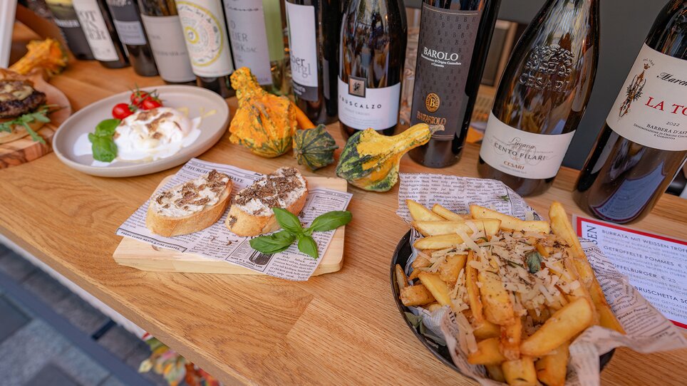 A selection of wines, truffle dishes, and sides on a wooden table. | © 5komma5sinne - Rene Strasser