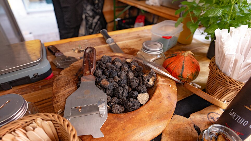A wooden bowl filled with fresh truffles and a truffle slicer on a wooden table. | © 5komma5sinne - Rene Strasser