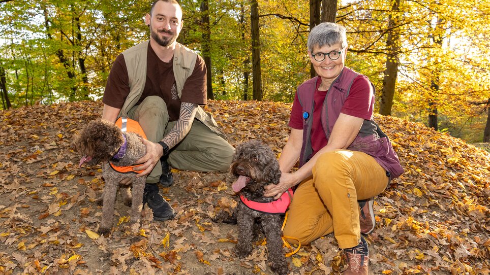 Ein Mann und eine Frau posieren mit zwei Hunden im Wald während des Herbsts. | © Graz Tourismus - Harry Schiffer