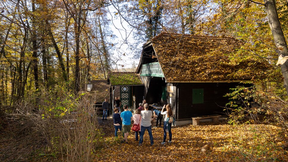 A group of people is looking at a cabin in the forest, surrounded by colorful autumn leaves. | © Graz Tourismus - Harry Schiffer