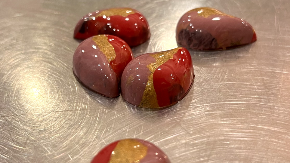 Fünf tropfenförmige Pralinen in Rot und Pink mit goldenen Akzenten. | © Jaimy Reisinger