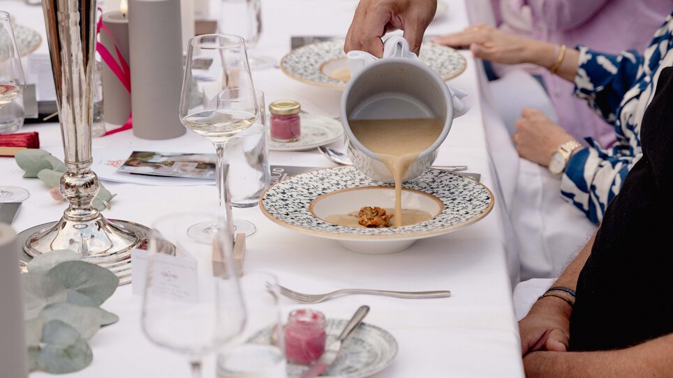 Eine Person gießt Suppe in einen Teller während eines festlichen Essens. | © Region Graz - www