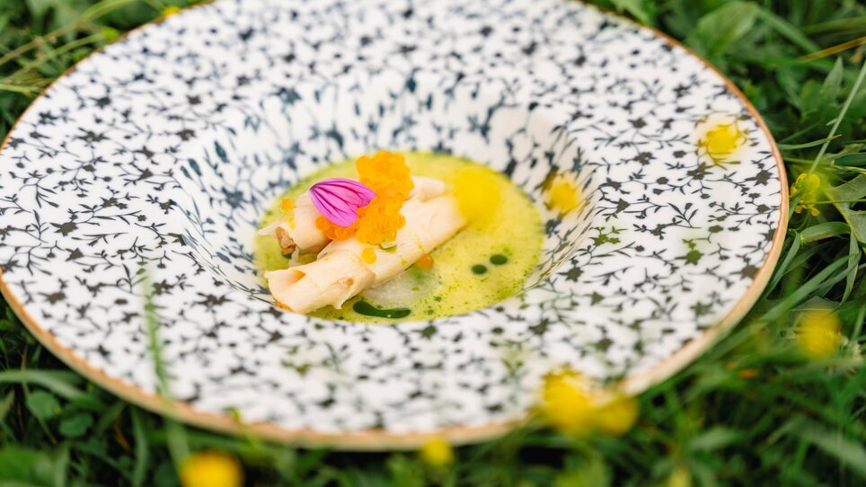 Ein kreatives Gericht in einem kunstvollen Teller, garniert mit Blüten und einer Sauce. | © Region Graz - Wolfgang Hummer