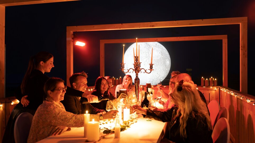 Eine festliche Dinnergesellschaft um einen Tisch mit Kerzen und Sekt, bei Nacht, unter einem großen Mond. | © Region Graz - Wolfgang Hummer