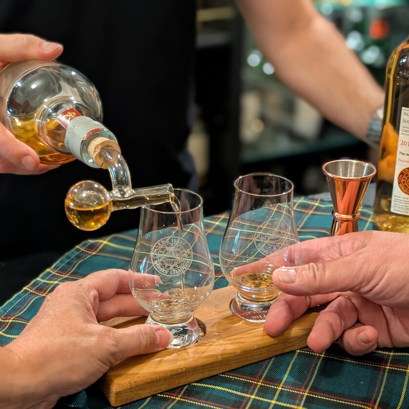 Zwei Gläser werden mit Whiskey gefüllt, während zwei Hände bereit sind. | © The Islay Whisky Chapter Austria