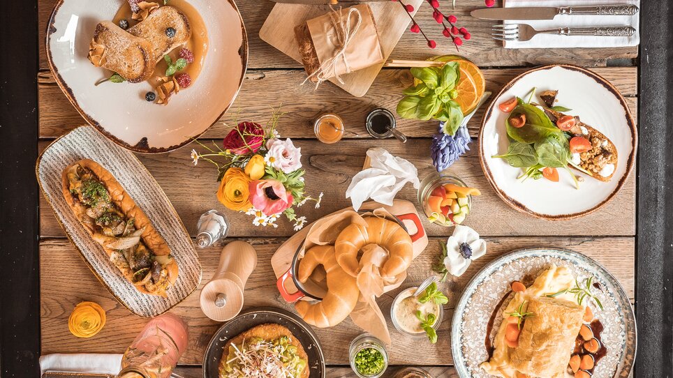 Variety of dishes, drinks, and floral arrangements on a wooden table. | © Kunsthaus Graz
