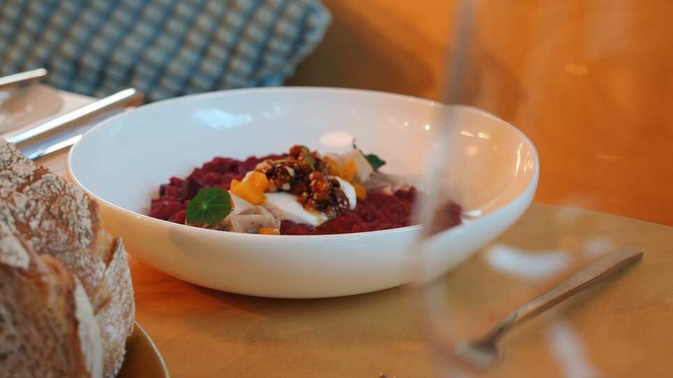 Eine Schüssel mit buntem Gericht und frischem Brot auf einem Tisch. Ganz in der Nähe steht ein Glas. | © Julia Riedesser - 1000things