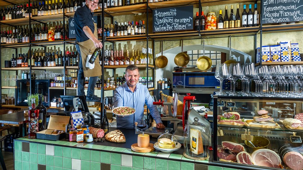 Zwei Männer in einem Restaurant, einer serviert Pasta, der andere hält eine Weinflasche. | © Paul Stajan