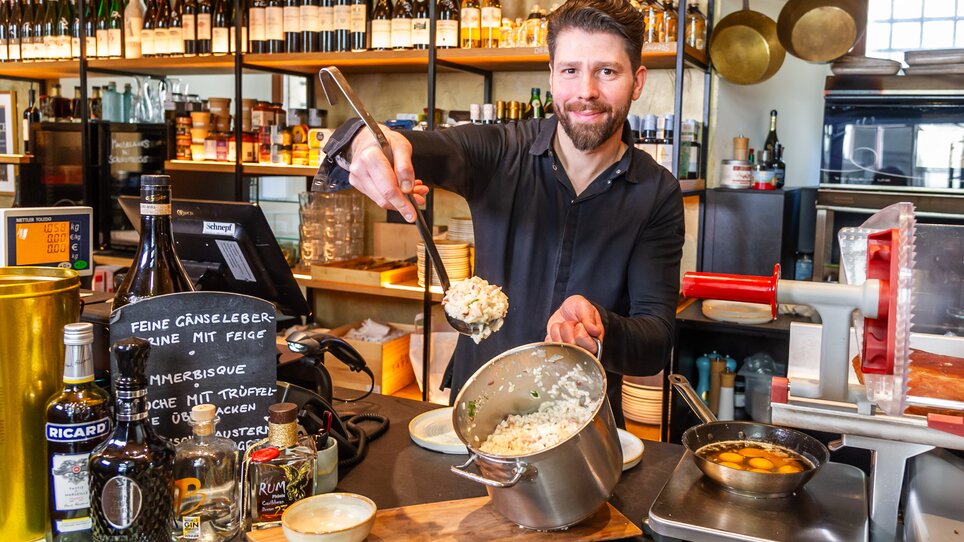 Mann serviert Gericht in einem Restaurant mit Weinregal. | © Paul Stajan