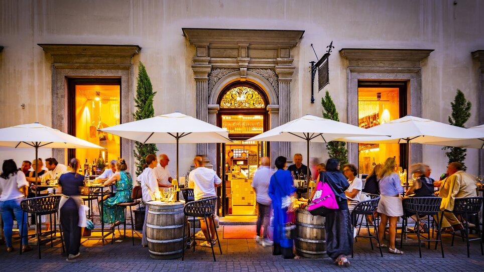Menschen genießen Essen und Trinken in einem Gastgarten vor einem Restaurant im Freien. | © Werner Krug