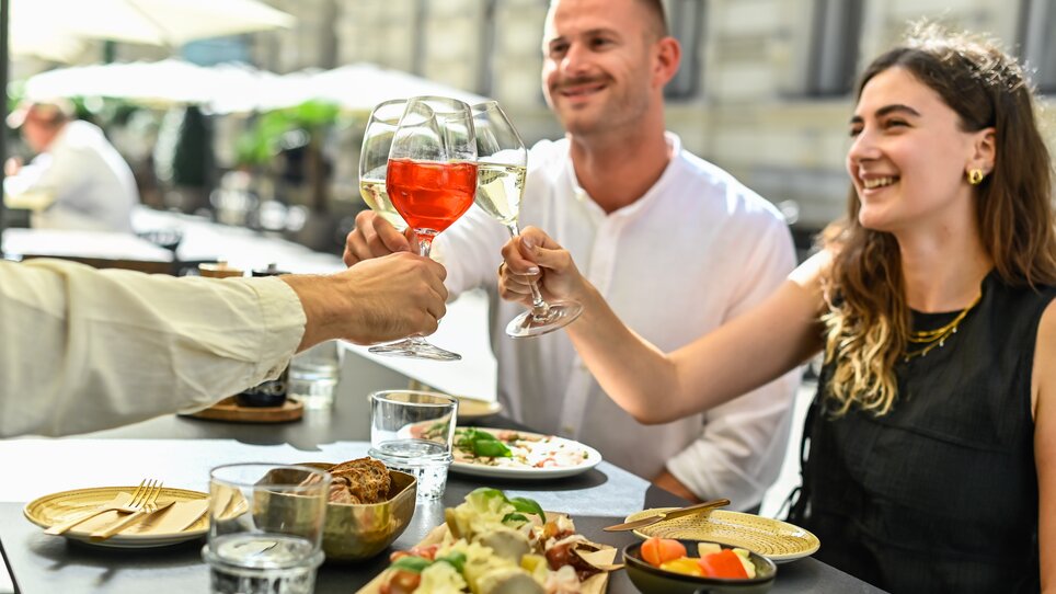 Freunde stoßen an einem Tisch mit Essen in Graz an. | © Paul Stajan