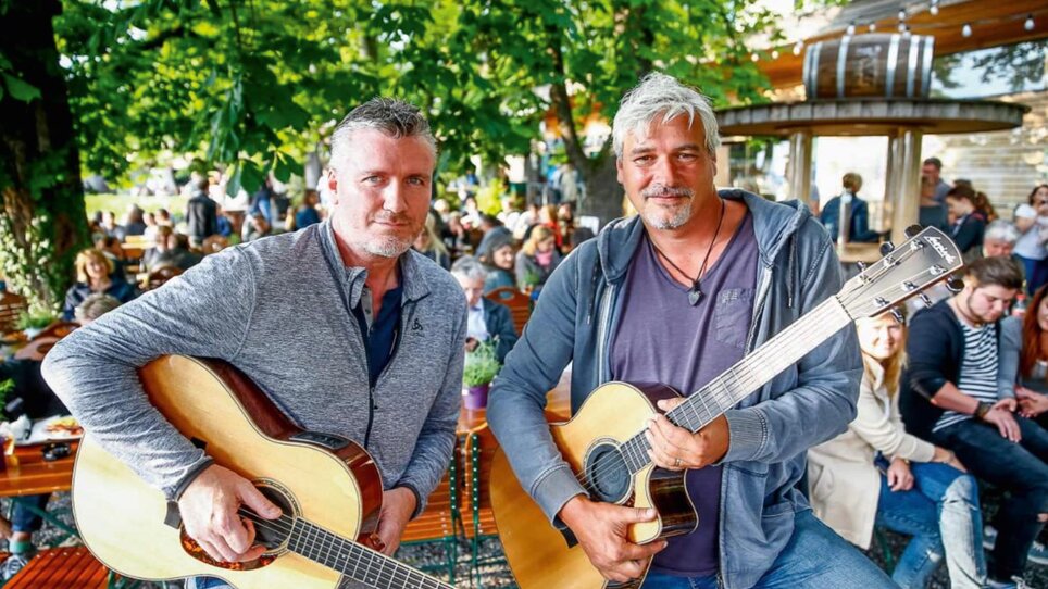 Two men with guitars pose for a photo in a green setting. | © Werner Krug