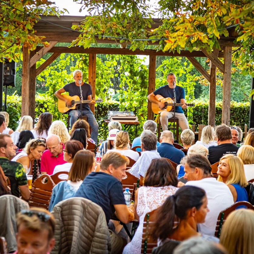 Restaurant SCHLOSSBERG I Essen & Trinken in Graz I DeZwa im Biergarten am Schlossberg | © Werner Krug Zwei Musiker spielen Akustikgitarre vor einem Publikum in einem Restaurant. | © Werner Krug