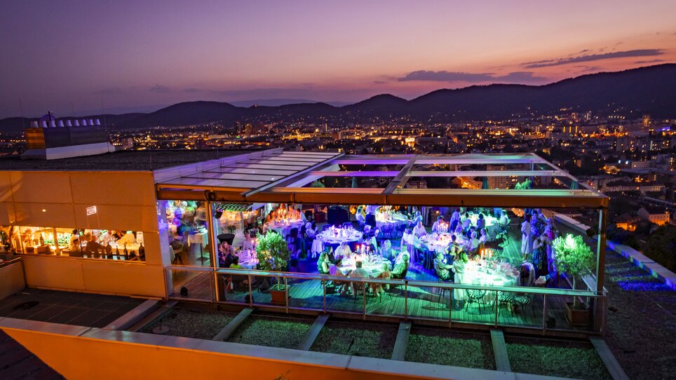 Das Restaurant SCHLOSSBERG mit Blick auf Graz bei Abenddämmerung.