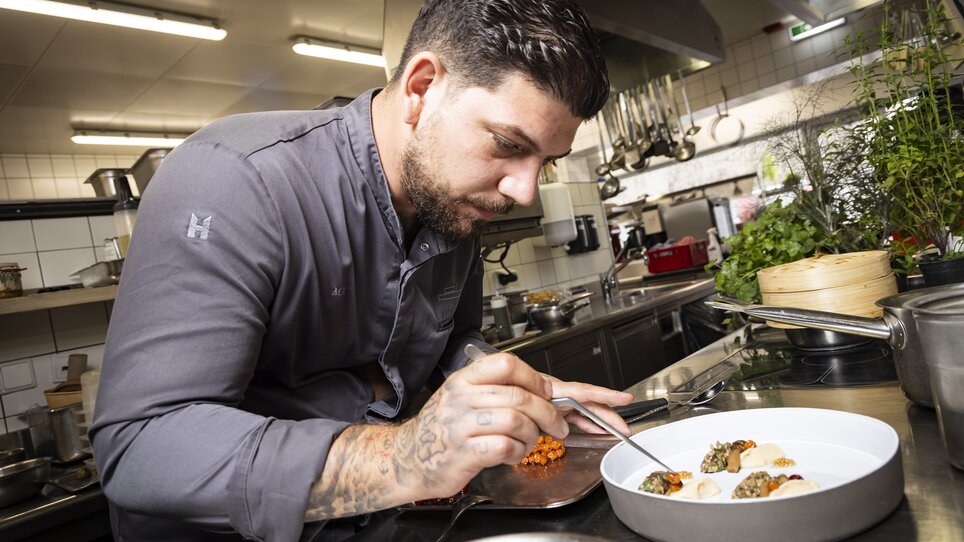 A chef garnishing a plate of food in a modern kitchen. | © Werner Krug