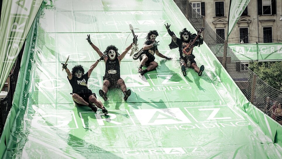 Verrückte Teilnehmer auf einer Rutsche beim Grazathlon. Besondere Kostüme und spaßige Atmosphäre. | © SportografCompanyCode