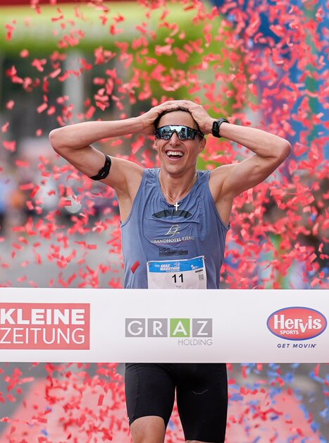 A runner celebrates victory at the Graz marathon, surrounded by confetti. | © GEPA