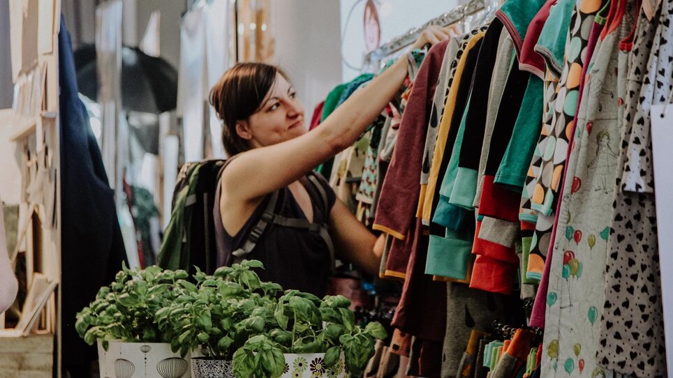Una donna esamina vestiti a uno stand del mercato dell'arte e del design. | © Kunst- und Designmarkt