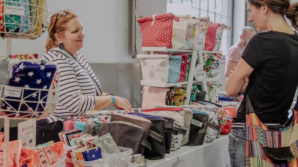 Una venditrice mostra borse in un mercato d'arte e design. | © Kunst- und Designmarkt