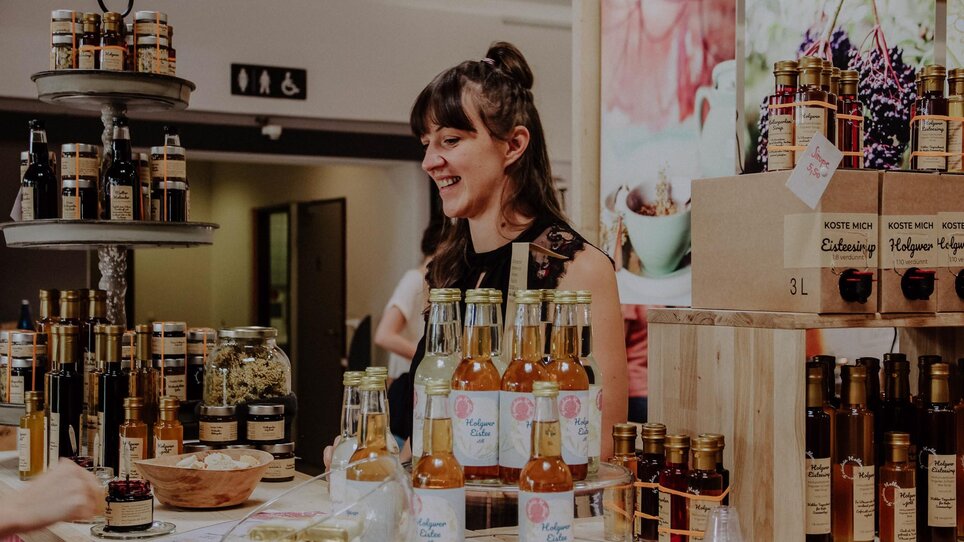 Una venditrice felice presenta i suoi prodotti al Mercato dell'arte e del design di Graz. | © Kunst- und Designmarkt