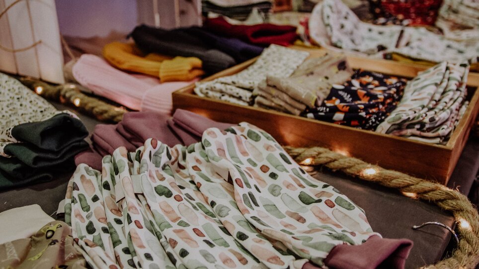 Tessuti e abbigliamento colorati su un tavolo al mercato dell'arte. | © Kunst- und Designmarkt