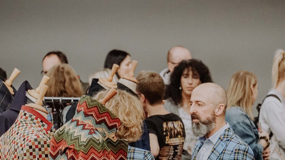 Visitatori a un mercato di arte e design con abbigliamento colorato.